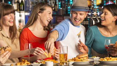 friends eating sandwiches and fries while drinking at bar